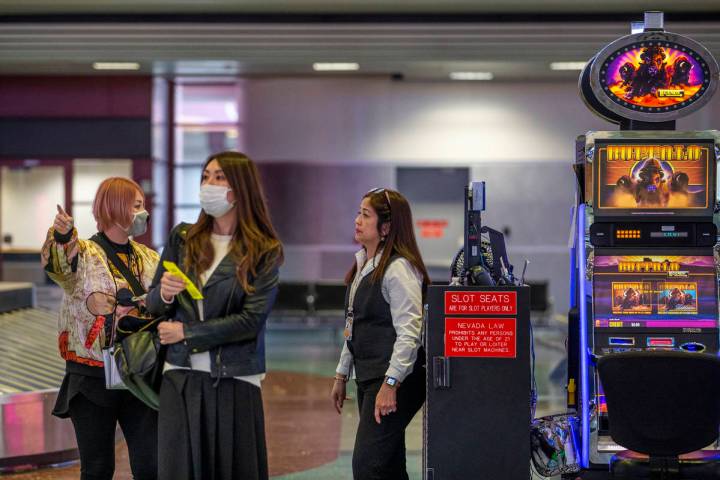 Masked passengers say for directions from slots employee Marites Mallari, right, in the baggage ...