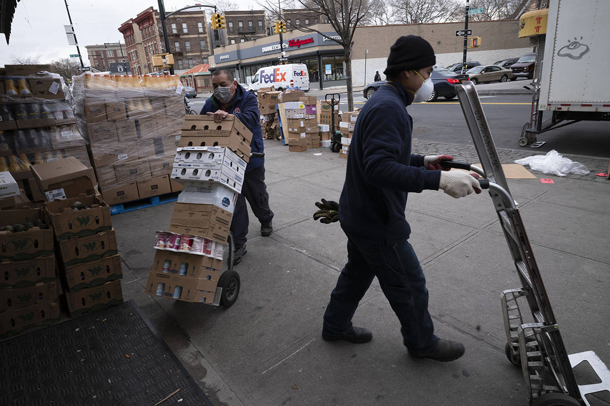 Supermarket workers wearing masks use hand carts to move food into the store during the coronav ...