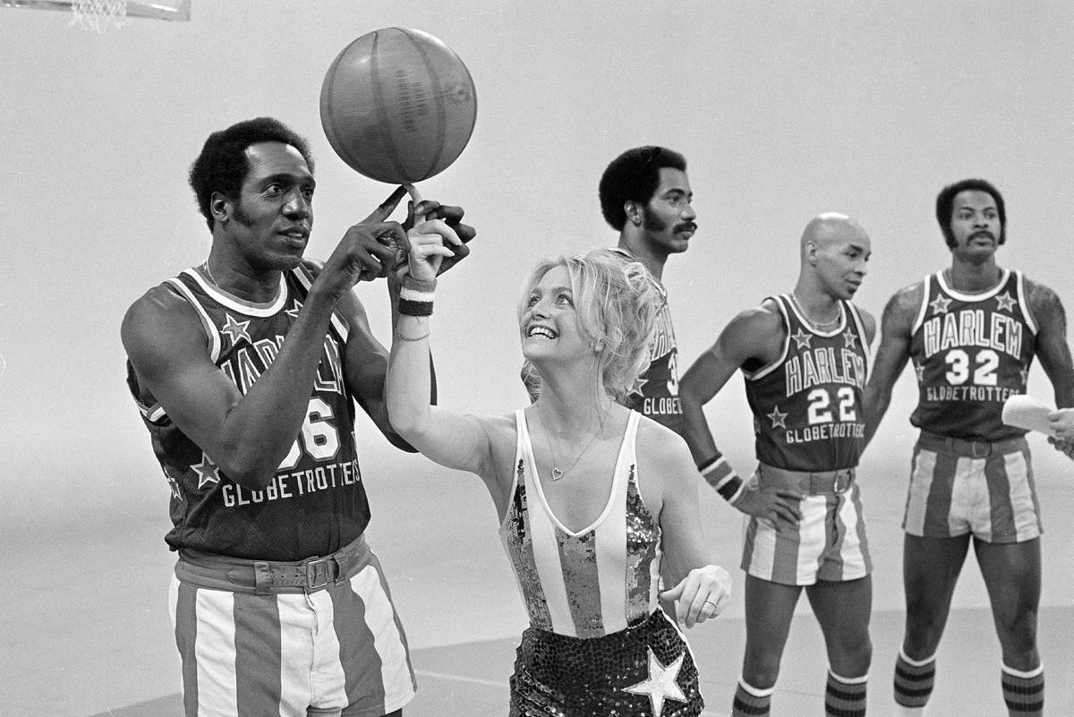 Actress Goldie Hawn has her finger guided to the basketball by Harlem Globetrotters' Meadowlark ...