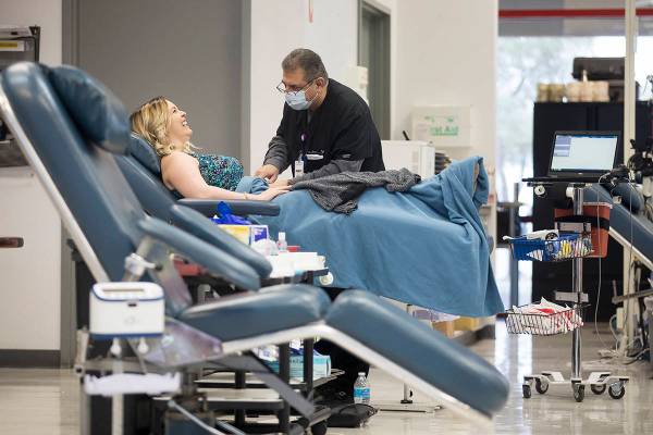 Donor Care Technician Tony Roybal, right, prepares Mary Beth Atanasiu, left, to give blood at V ...