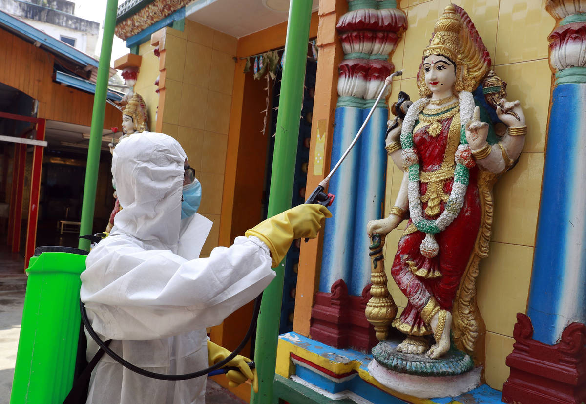 A member of the military wearing full protective gear sprays disinfectant at a Hindu temple to ...