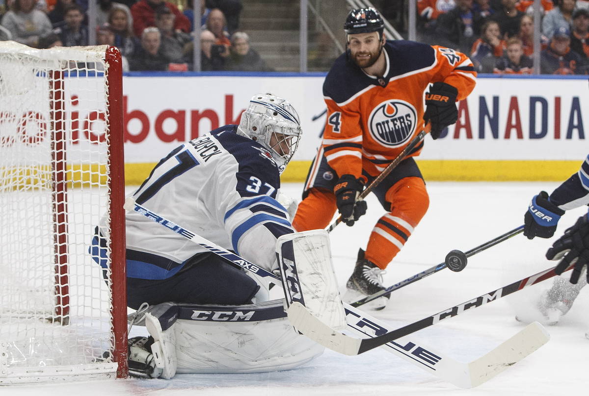 Winnipeg Jets goalie Connor Hellebuyck (37) makes a save as Edmonton Oilers' Zack Kassian (44) ...