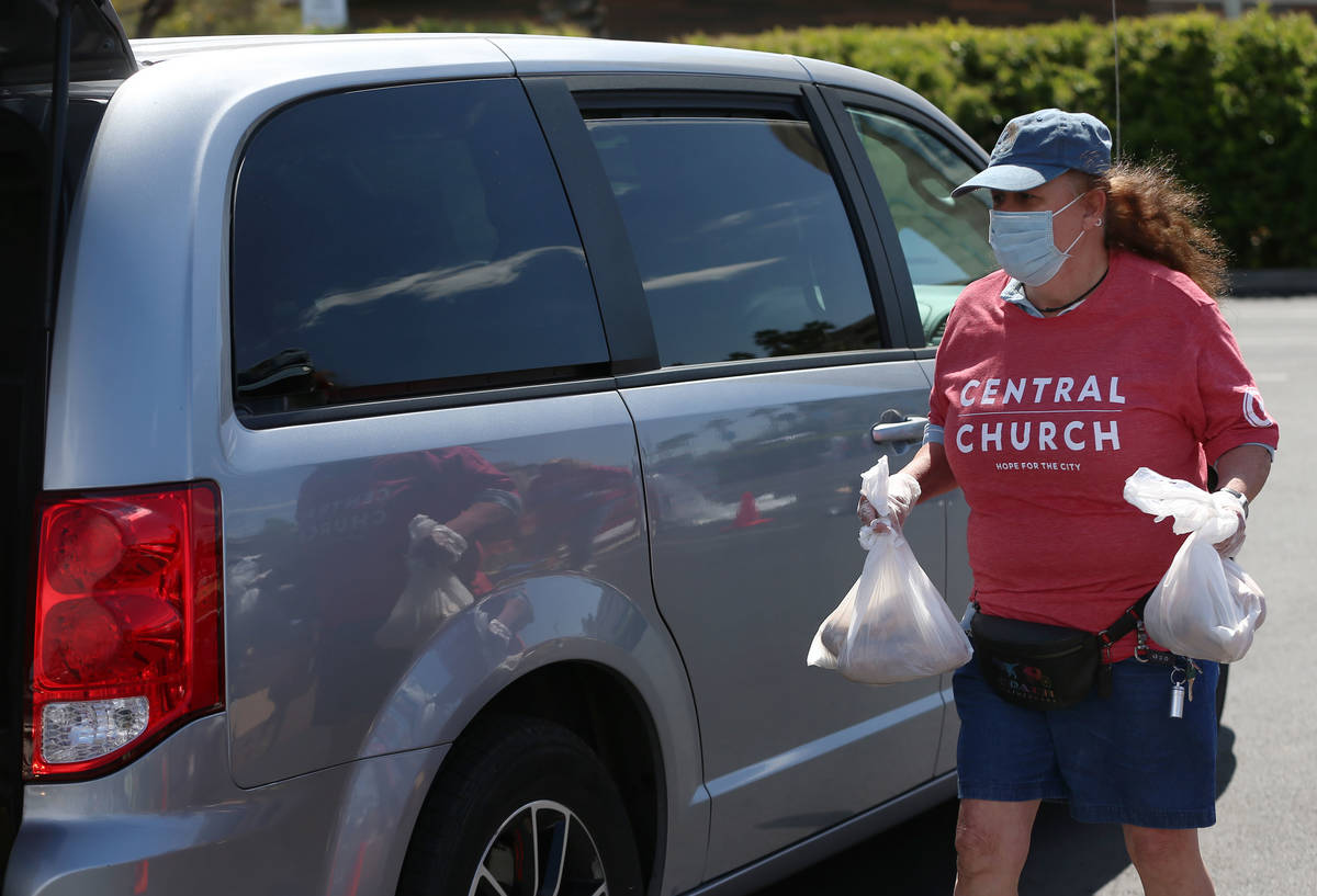 Three Square Food Bank volunteer Michele Santiwan hands out food to people waiting in their car ...