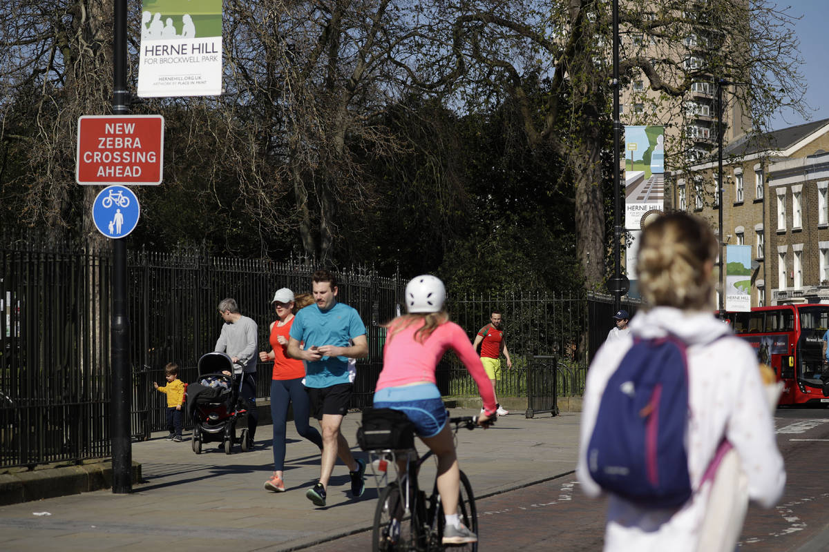 People observe social distancing as they pass by the locked gates to Brockwell Park in London, ...