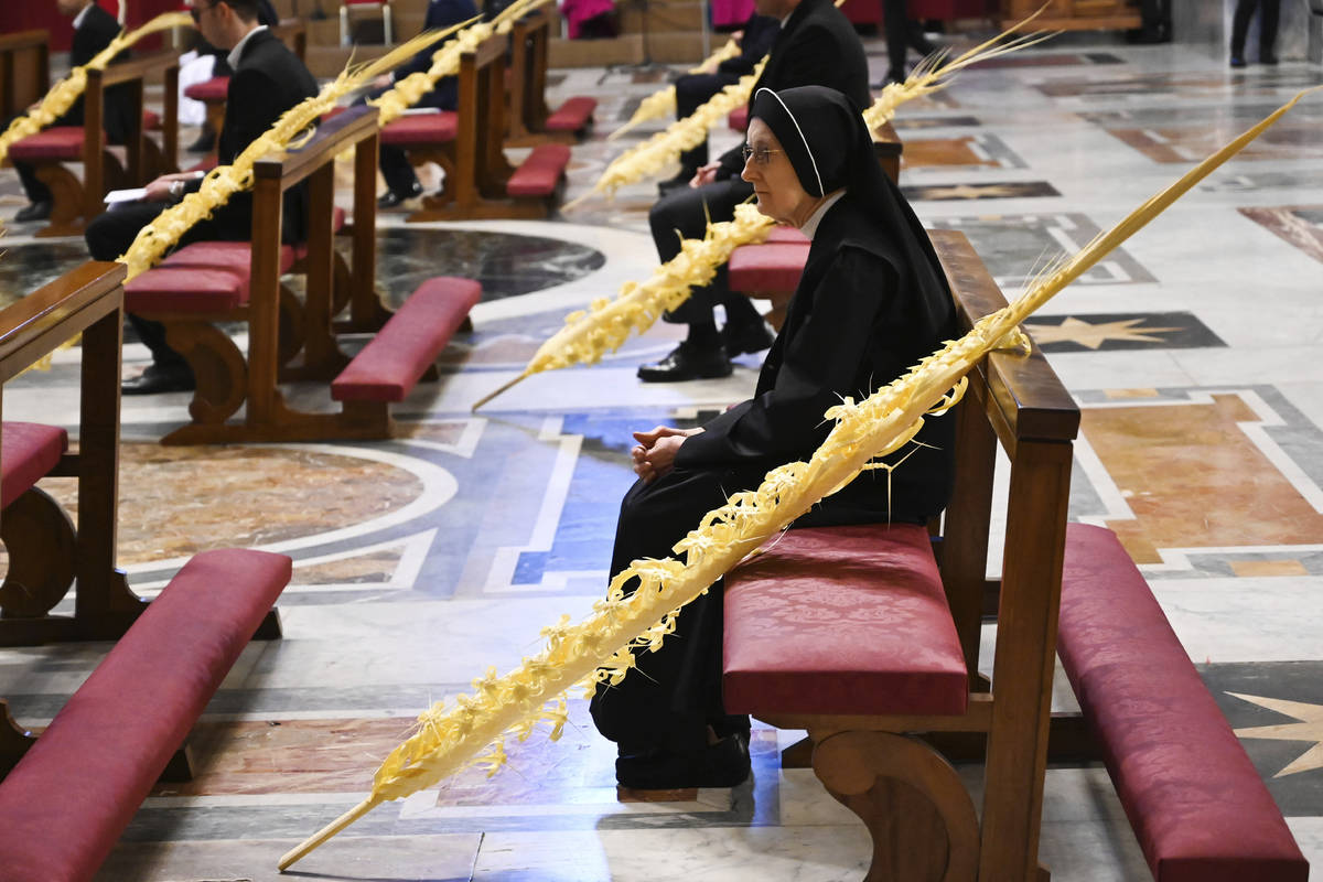 A nun sitting by a palm branch attends the Pope's Palm Sunday Mass behind closed doors in St. P ...