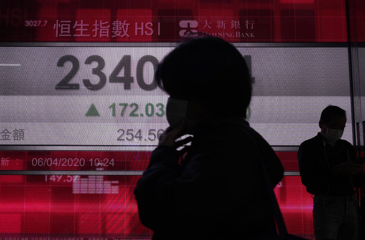 People wearing face masks walk past a bank electronic board showing the Hong Kong share index a ...