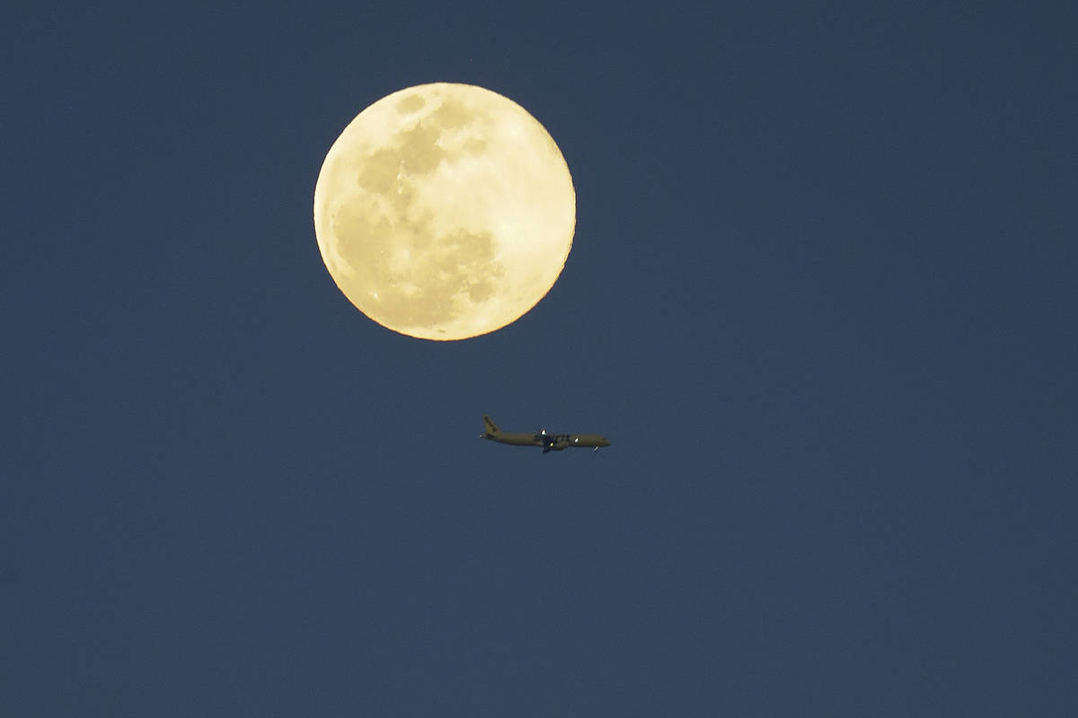 An airplane flys past a supermoon as it rises in the sky Tuesday, April 7, 2020, in Orlando, Fl ...