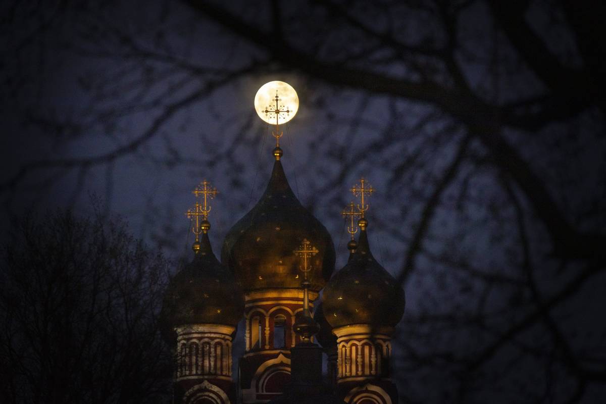 The supermoon rise behind an illuminated cross from a Christian Orthodox church in Moscow, Russ ...