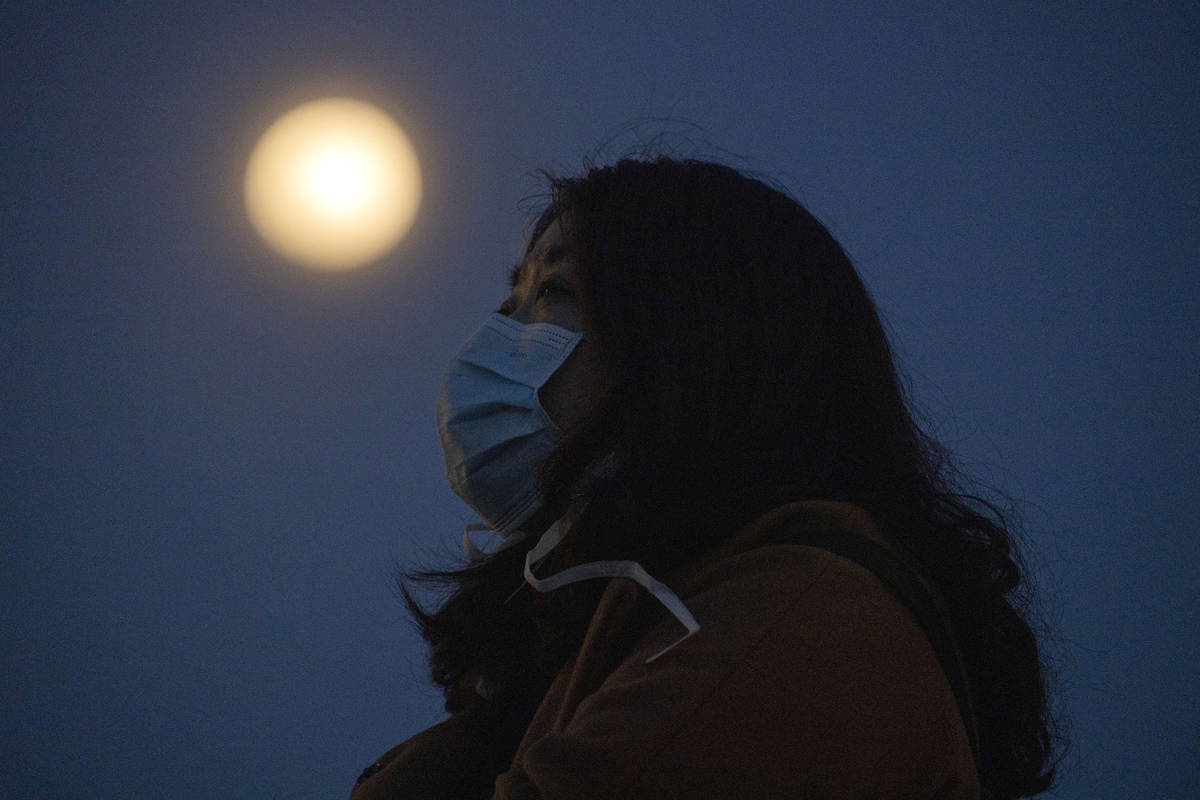 In this Monday, April 6, 2020, photo, a woman wearing a mask against the coronavirus looks up n ...