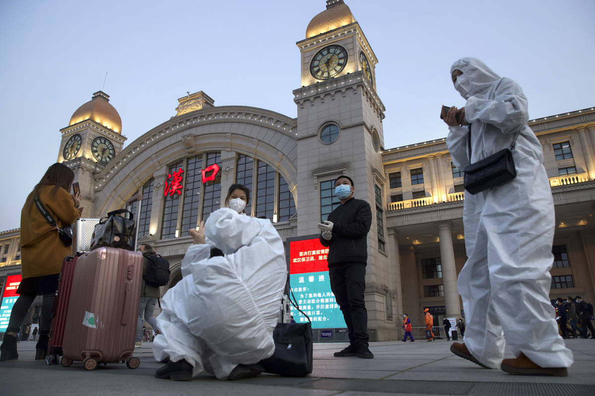 Passengers wearing protective suits to protect against the spread of new coronavirus gather out ...