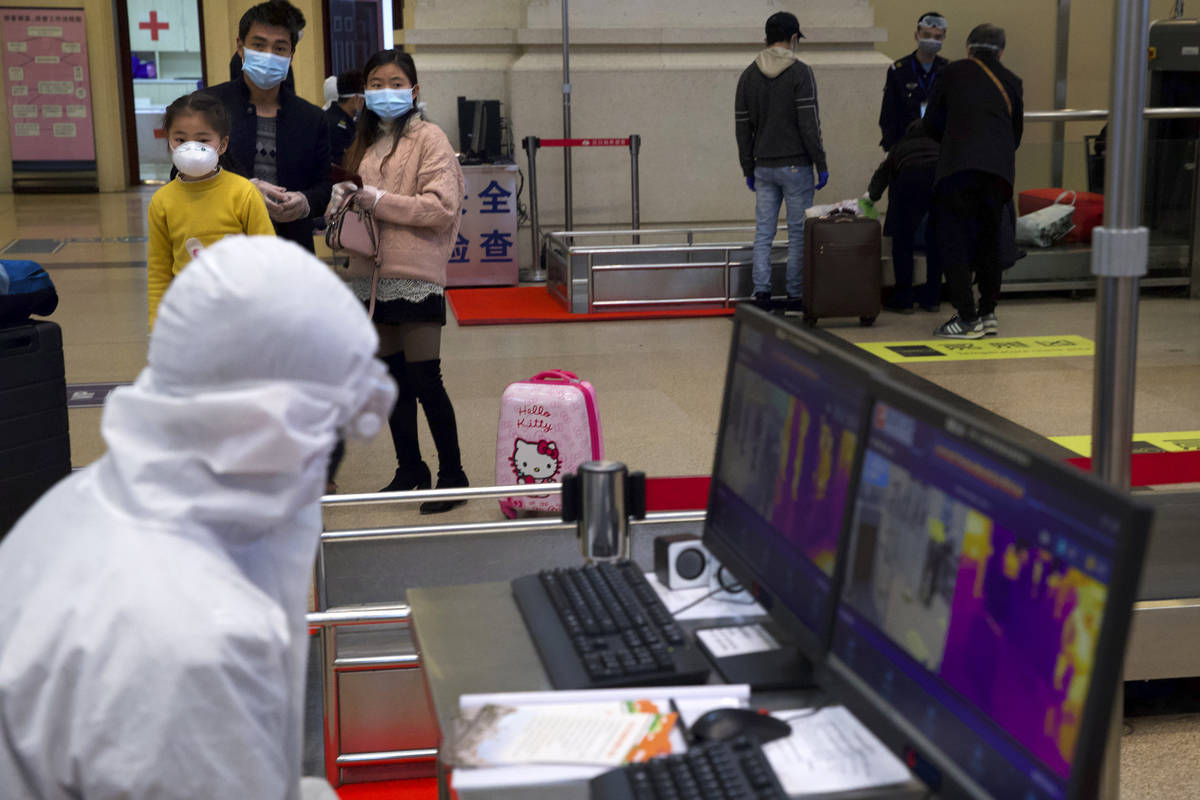 Passengers wearing face masks to protect against the spread of new coronavirus watch as a worke ...