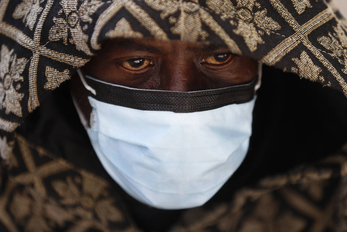 A man wears a protective mask while waiting for a bus in Detroit, Wednesday, April 8, 2020. Det ...