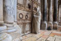 A Christian worshiper stands at the closed door of the Church of the Holy Sepulchre, believed b ...