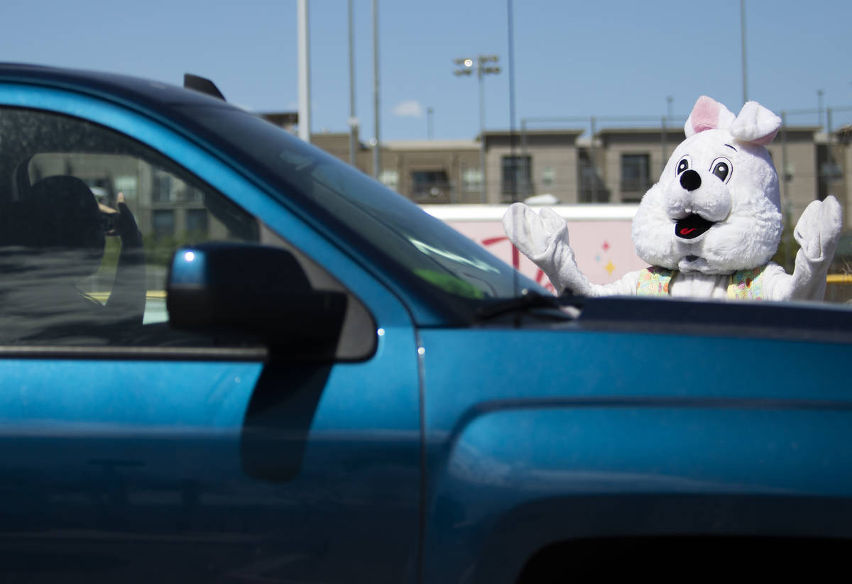 The Easter Bunny waves as cars proceed through an Easter basket drive through at Mountain Ridge ...