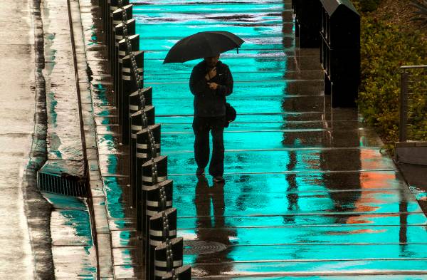 A pedestrian is bathed in blue light from a lighted sign above as he walks in the rain about th ...