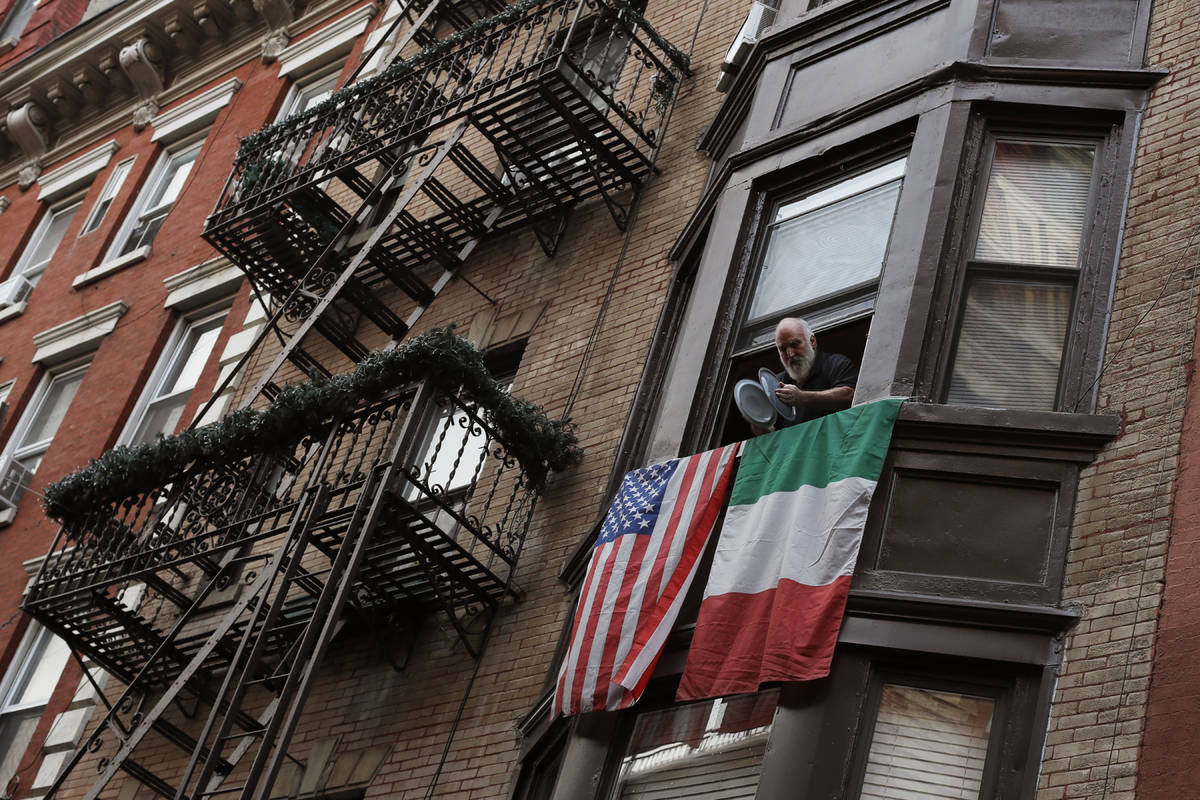 A man leans out the window on Mulberry Street in New York's Little Italy and bangs together pot ...