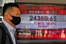 A masked man walks past an electronic board showing Hong Kong share index outside a local bank ...