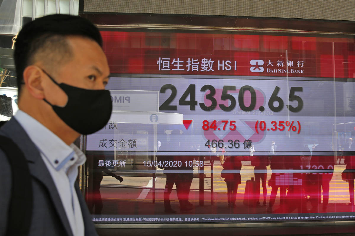 A masked man walks past an electronic board showing Hong Kong share index outside a local bank ...