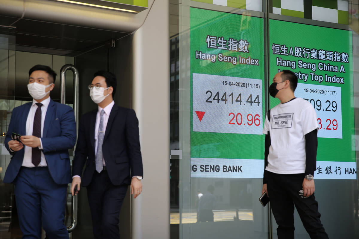 People wearing face masks walk past an electronic board showing Hong Kong share index outside a ...