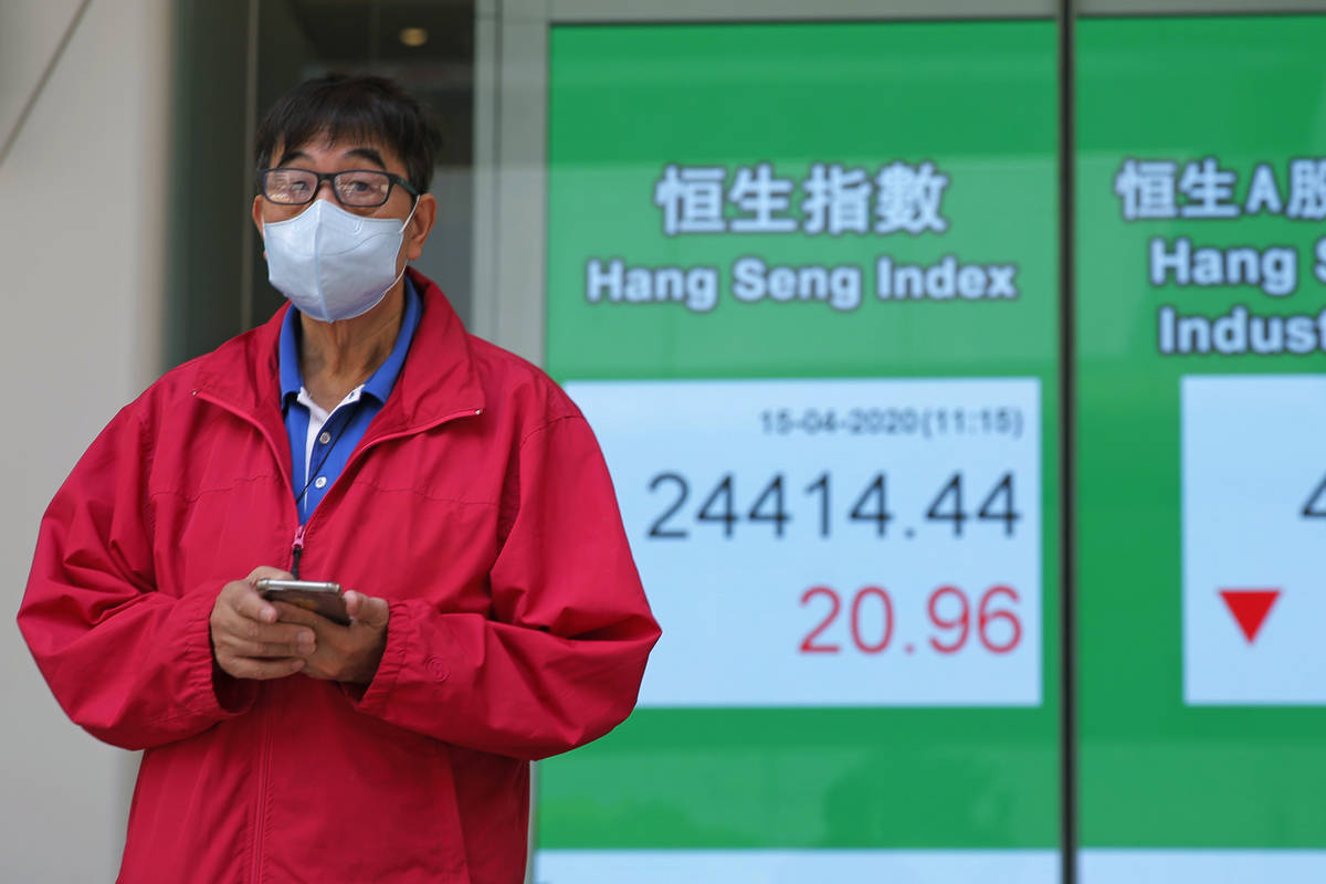 A masked man stands in front of an electronic board showing Hong Kong share index outside a loc ...