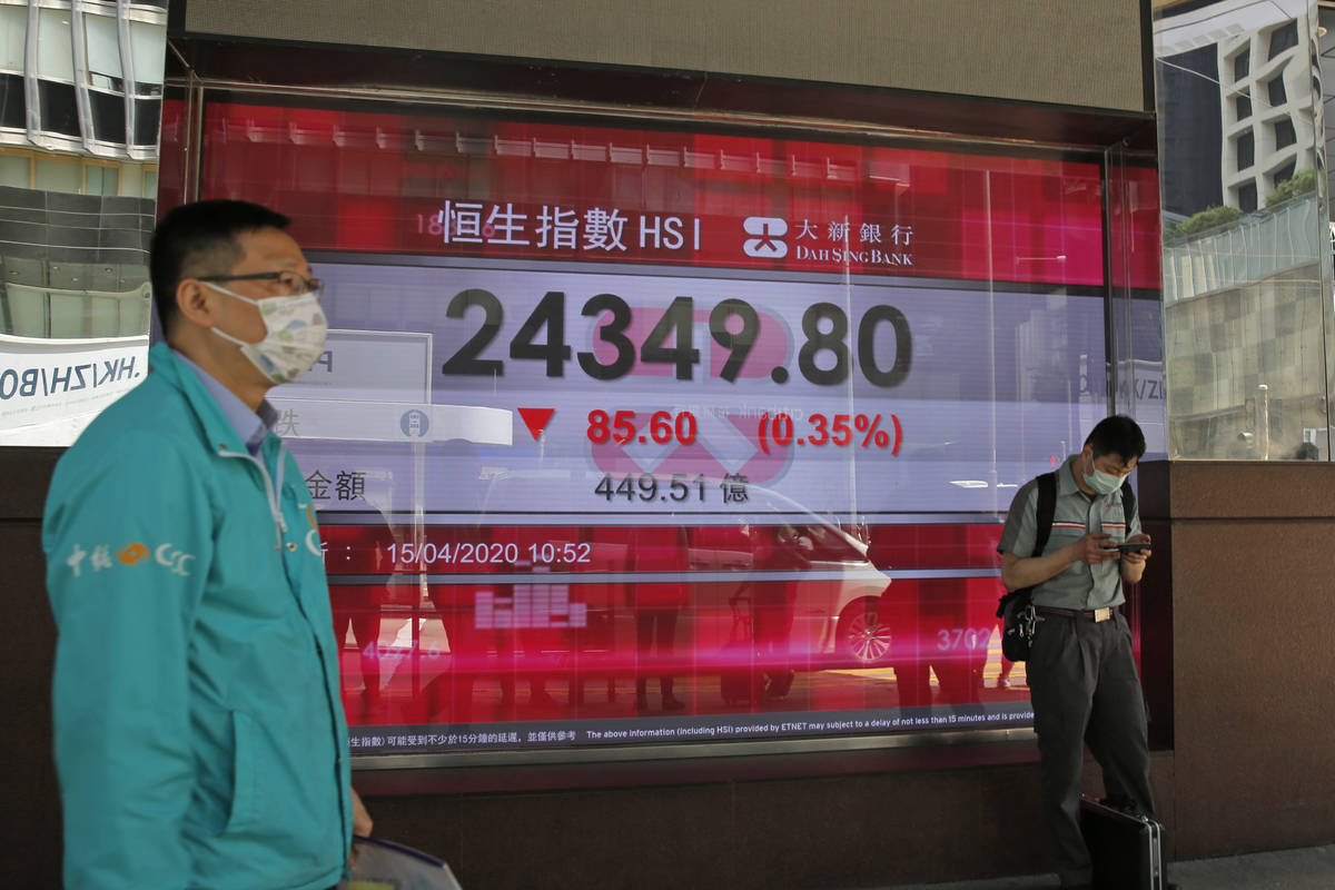 Men wearing face masks stand in front of an electronic board showing Hong Kong share index outs ...