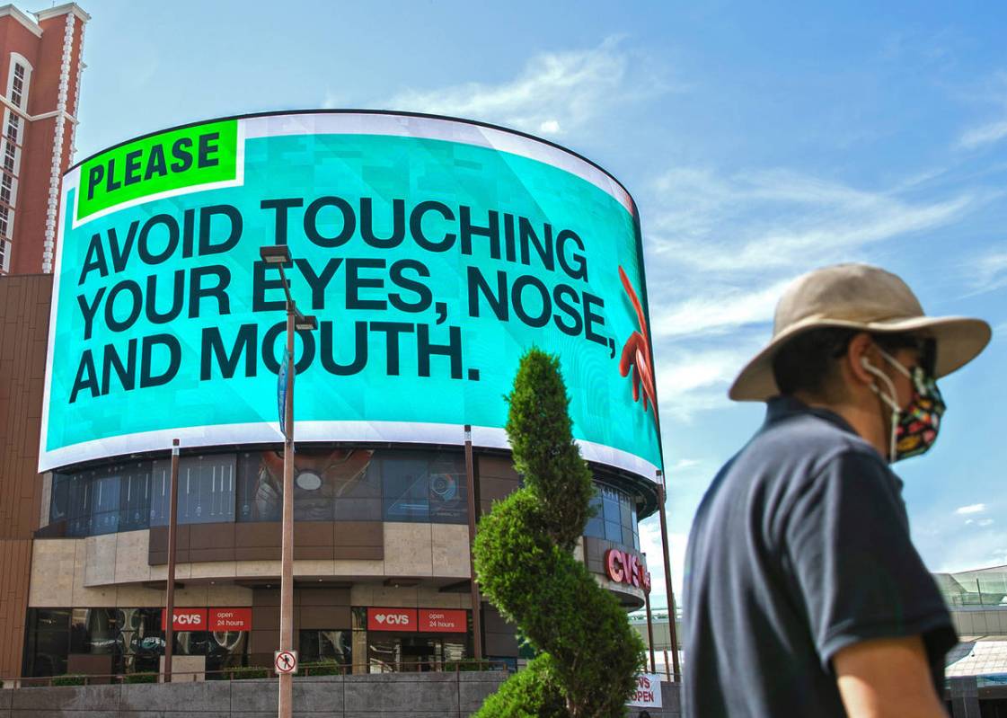 A pedestrian passes a large billboard addressing how to prevent the spread of the coronavirus ...