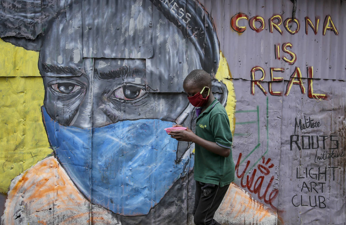 A boy wearing a face mask carries a small bowl of "githeri", or mixed beans and maize ...