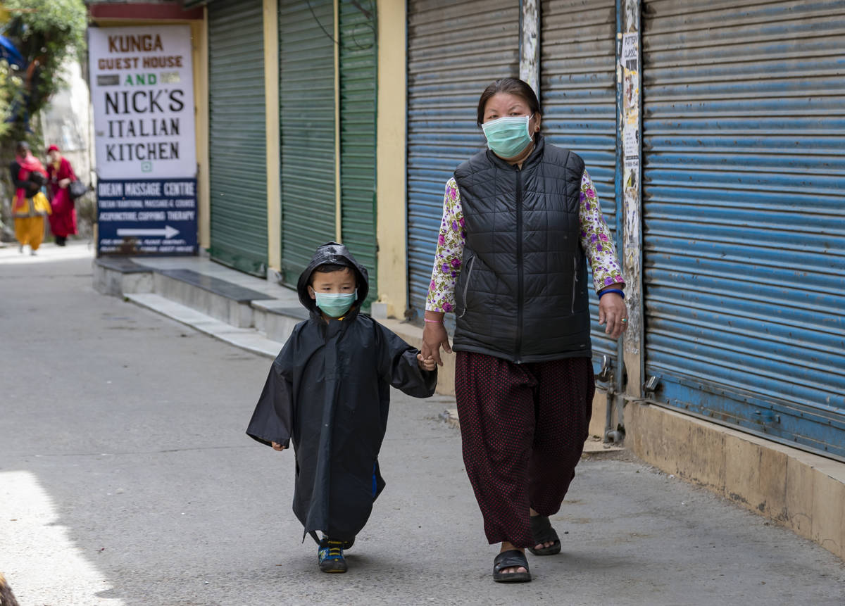 A child is covered in a raincoat and mask to protect him from coronavirus infection as he walks ...