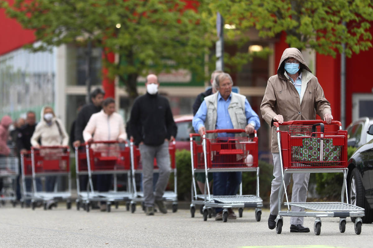 People wearing protective masks queue up to go in a garden store in Munich, Germany, Monday, Ap ...