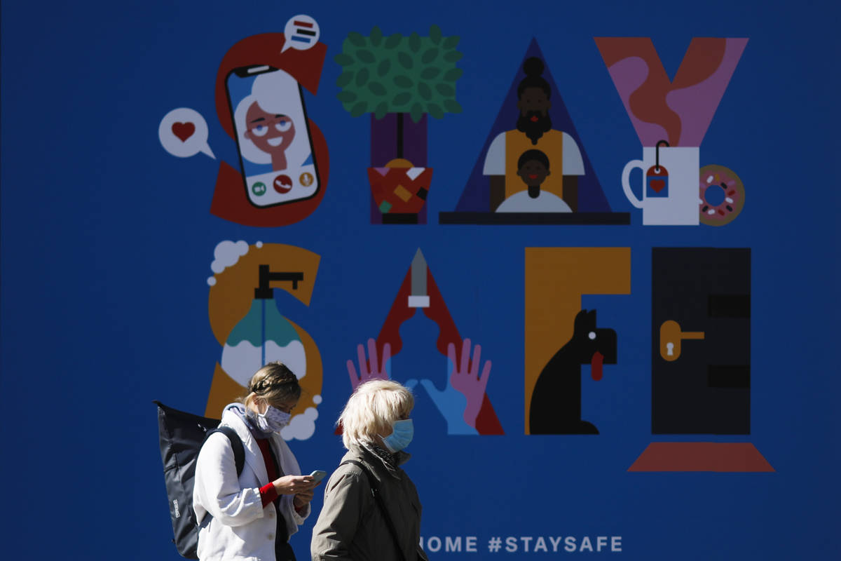 Two women with face masks stand in front of a poster at a department store in Berlin, Germany, ...