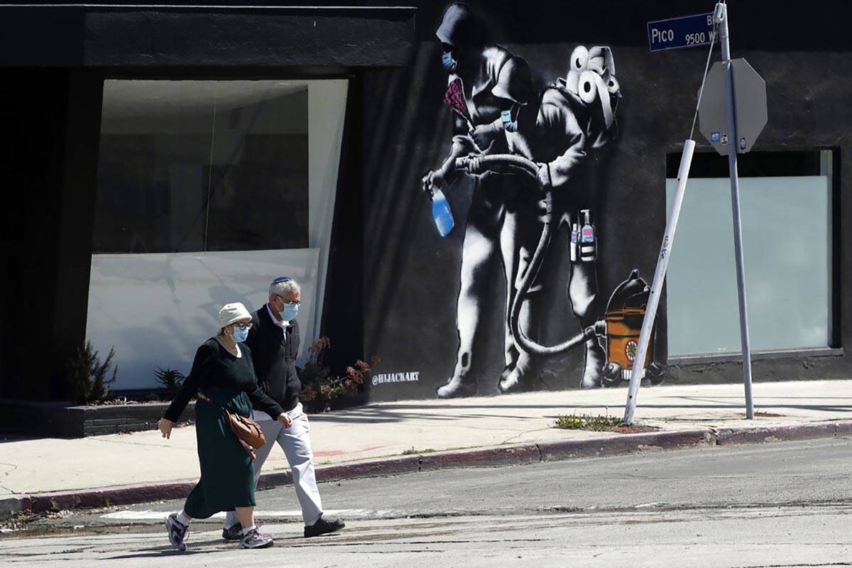 People wearing masks walk past a mural depicting a coronavirus theme during the COVID-19 pandem ...