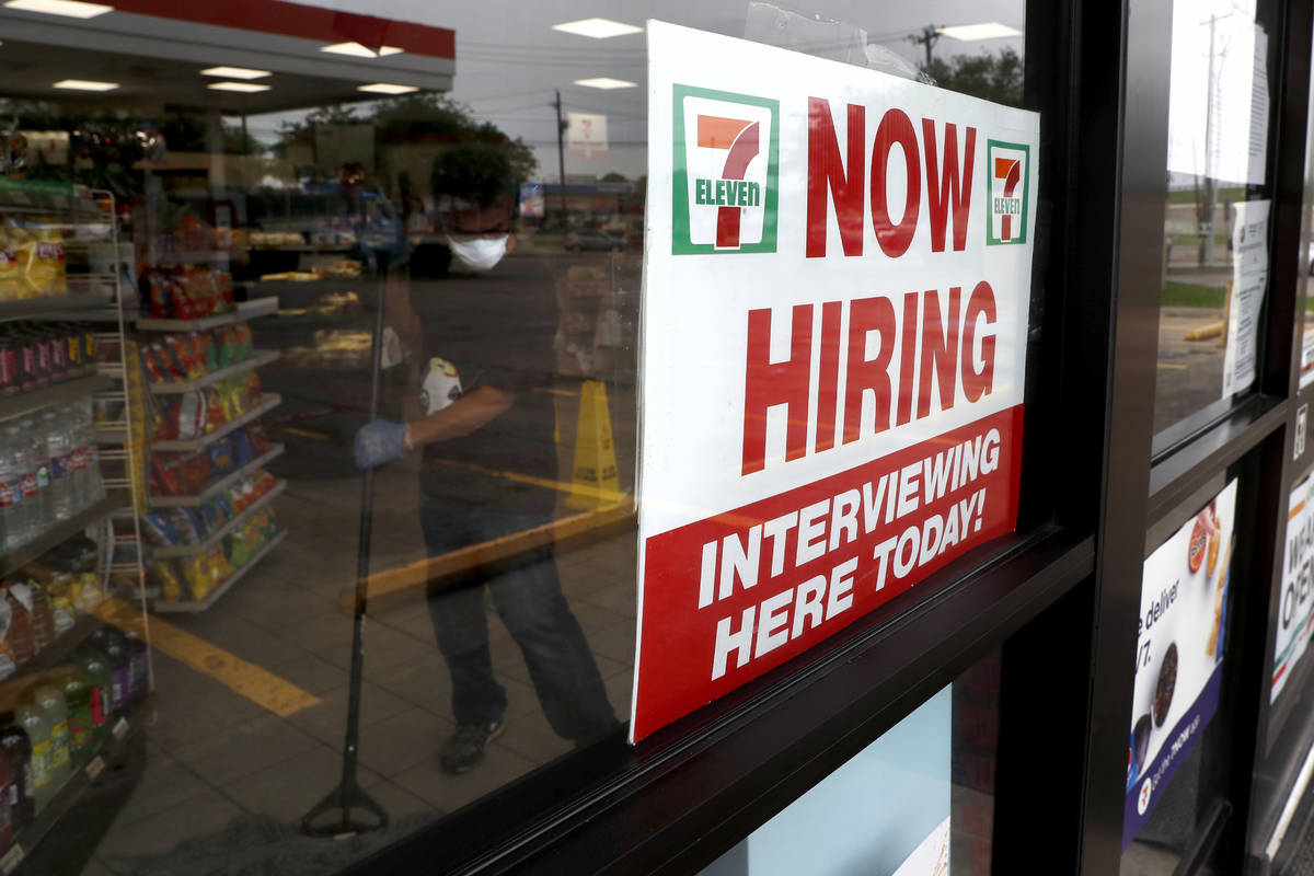 A sign on the window at a 7-Eleven store reads, "Now Hiring," as an employee inside t ...