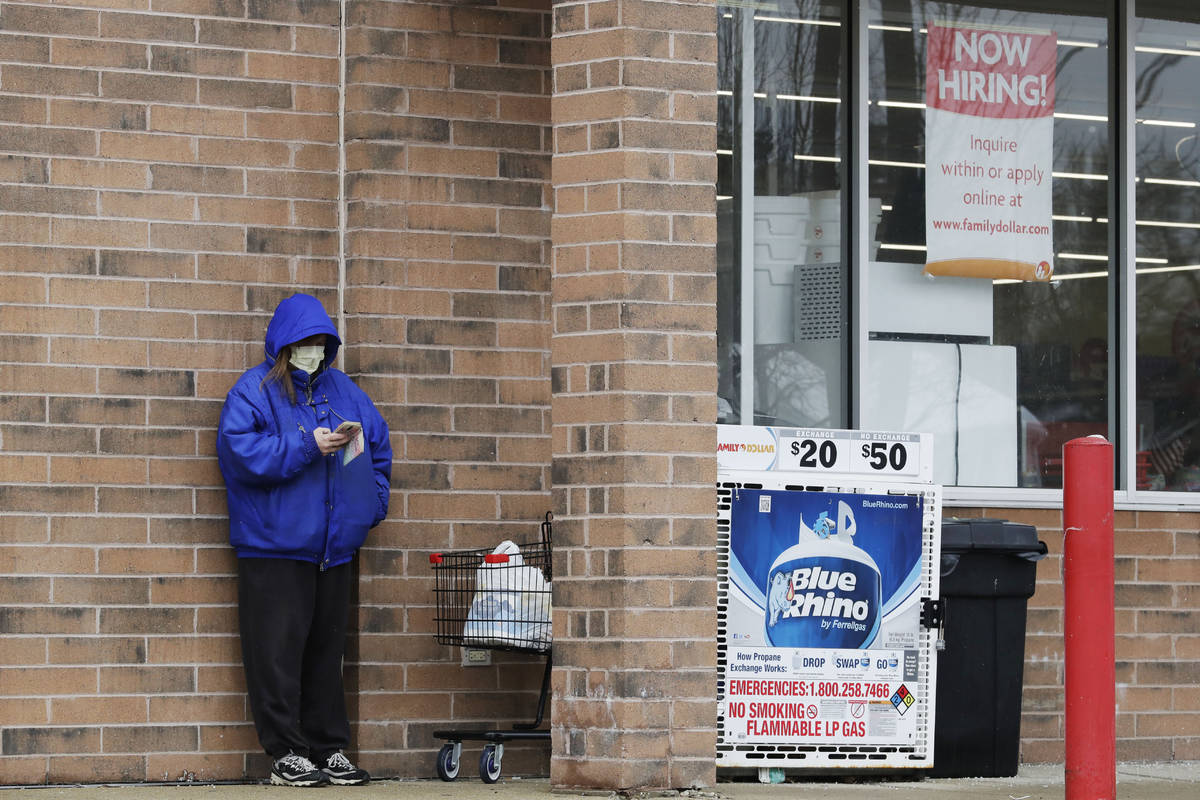 A woman checks her phone as a hiring sign shows at a Family Dollar store in Joliet, Ill., Frida ...