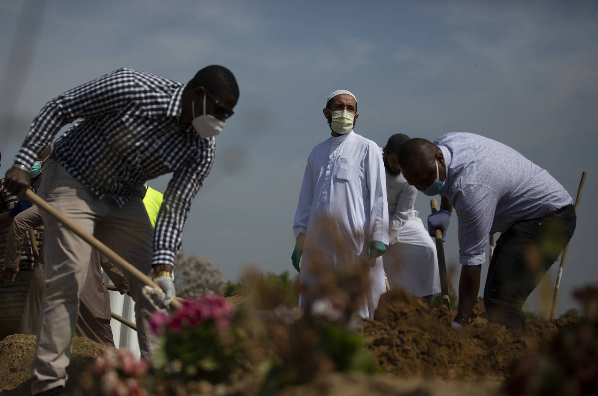 Mourners shovel dirt onto the grave of a Guinean man, who died of COVID-19 and who the family d ...