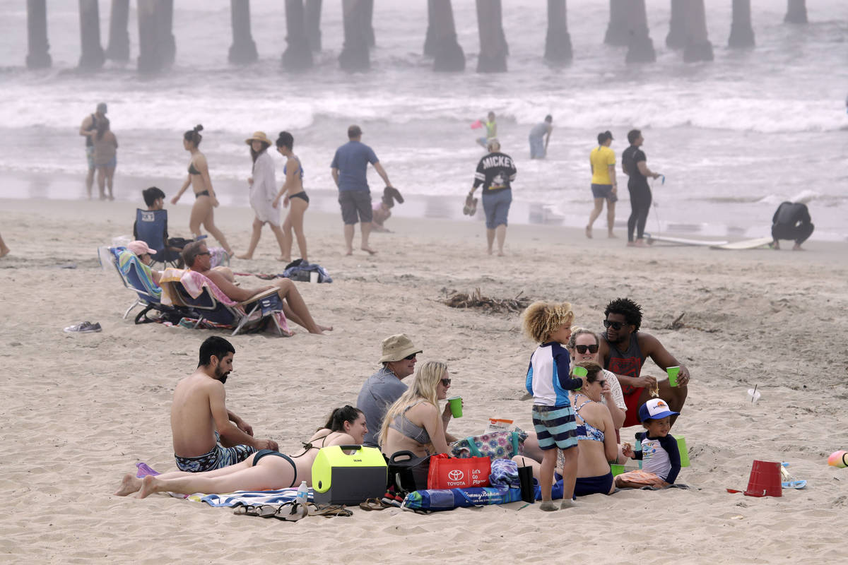 People sit on the beach Sunday, April 26, 2020, in Huntington Beach, Calif. (AP Photo/Marcio Jo ...