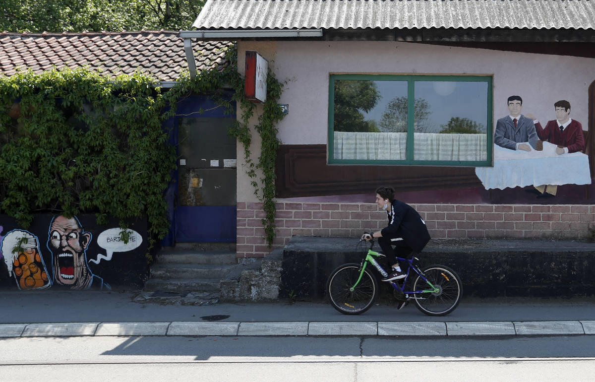 A boy rides a bicycle past a closed restaurant in Belgrade, Serbia, Monday, April 27, 2020. The ...