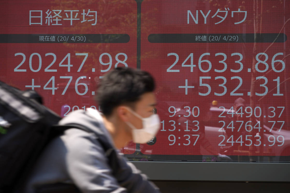A food delivery person rides a bicycle past an electronic stock board showing Japan's Nikkei 22 ...