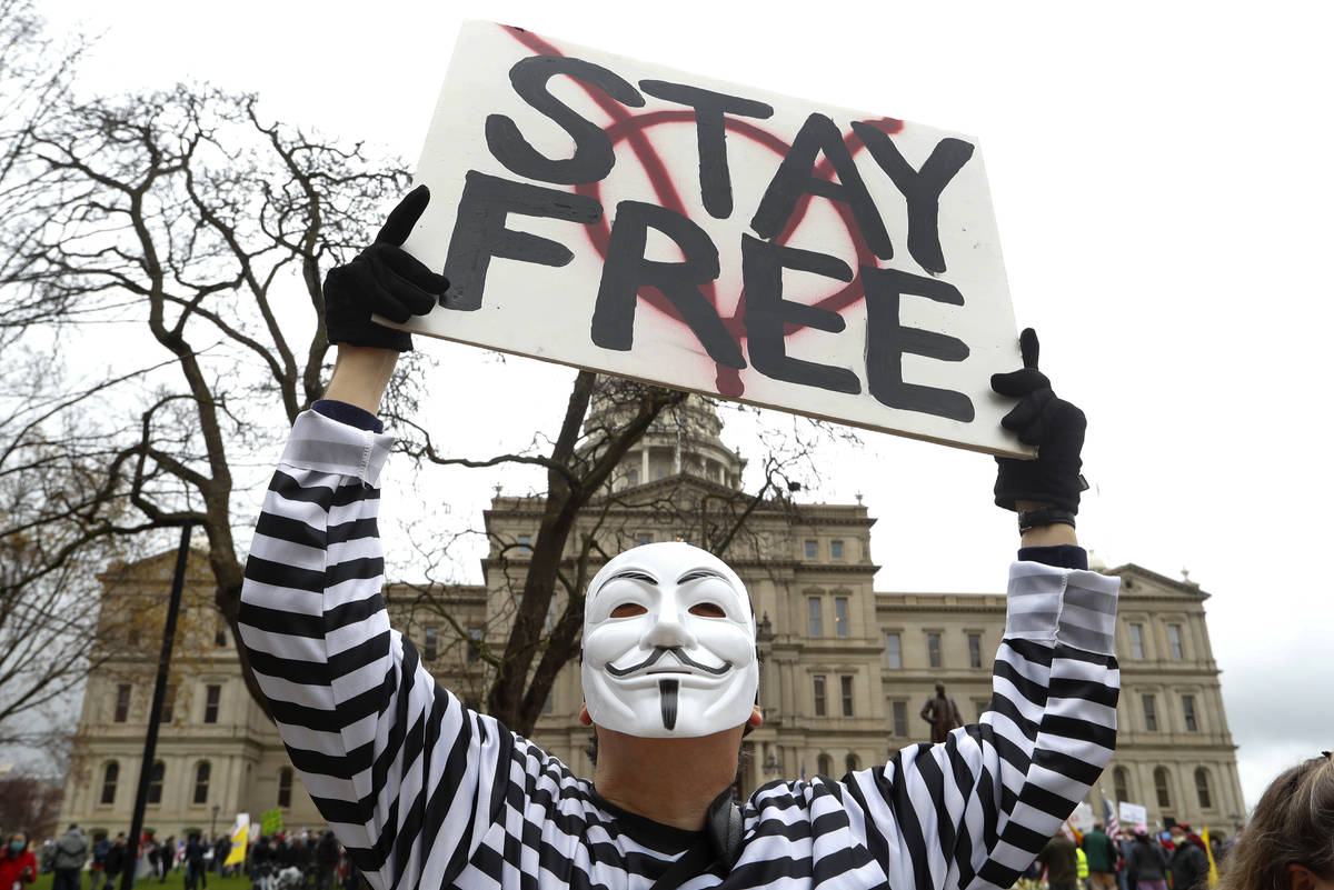 A protester holds a sign at the State Capitol in Lansing, Mich., Thursday, April 30, 2020. Hois ...
