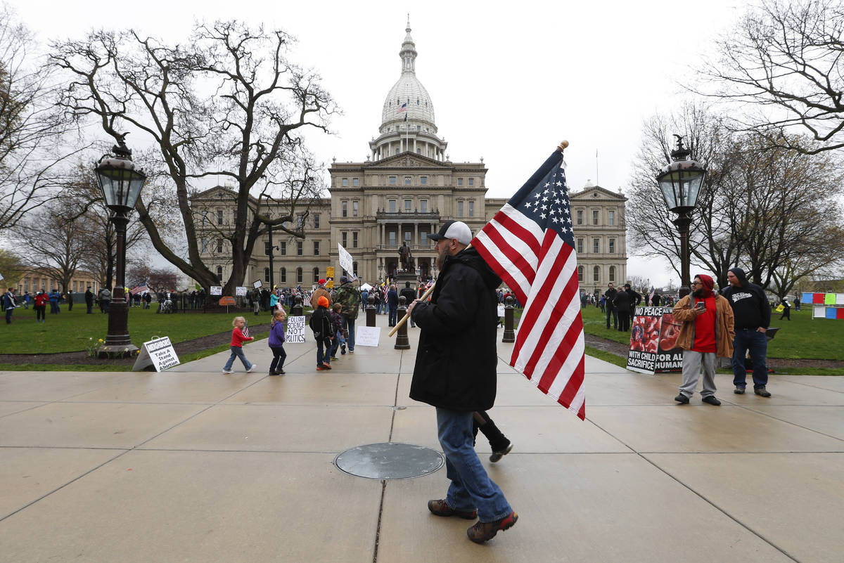 A protester carries an American flag at the State Capitol in Lansing, Mich., Thursday, April 30 ...