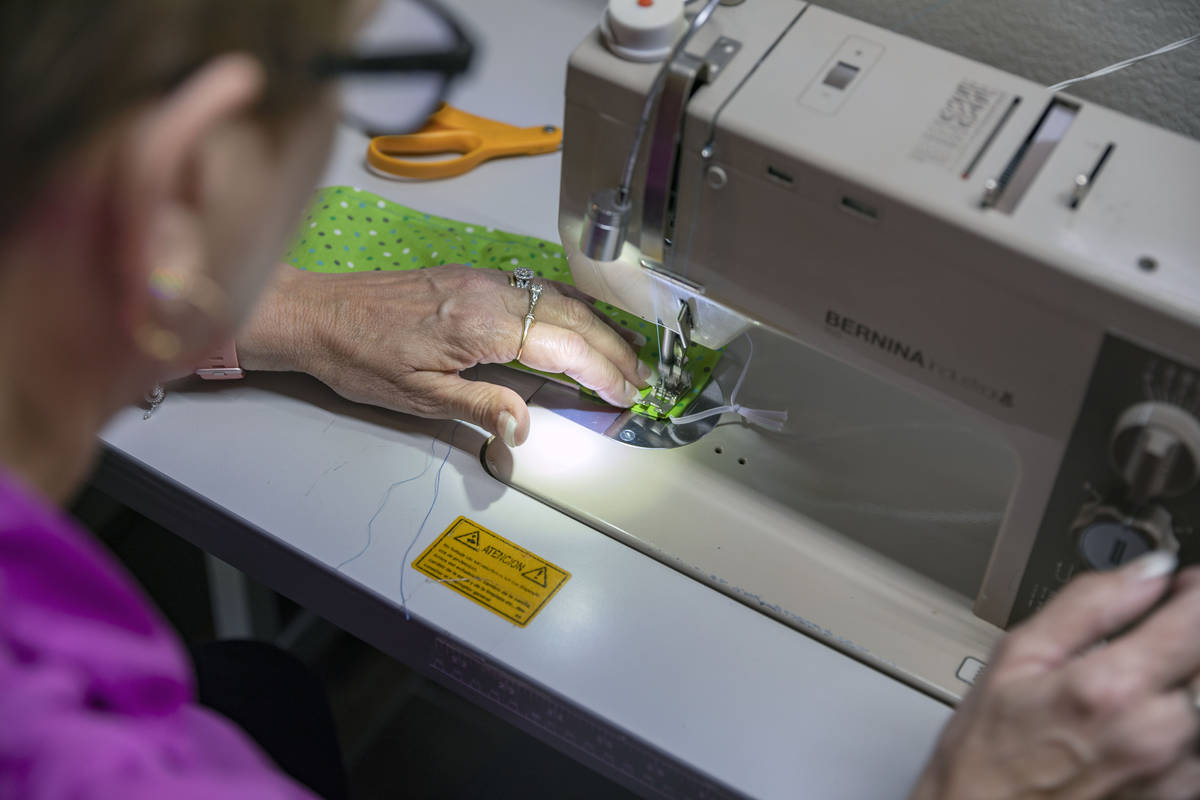 Michele Walker, owner of Imaginations Unlimited, sews a cloth face covering, in her embroidery ...