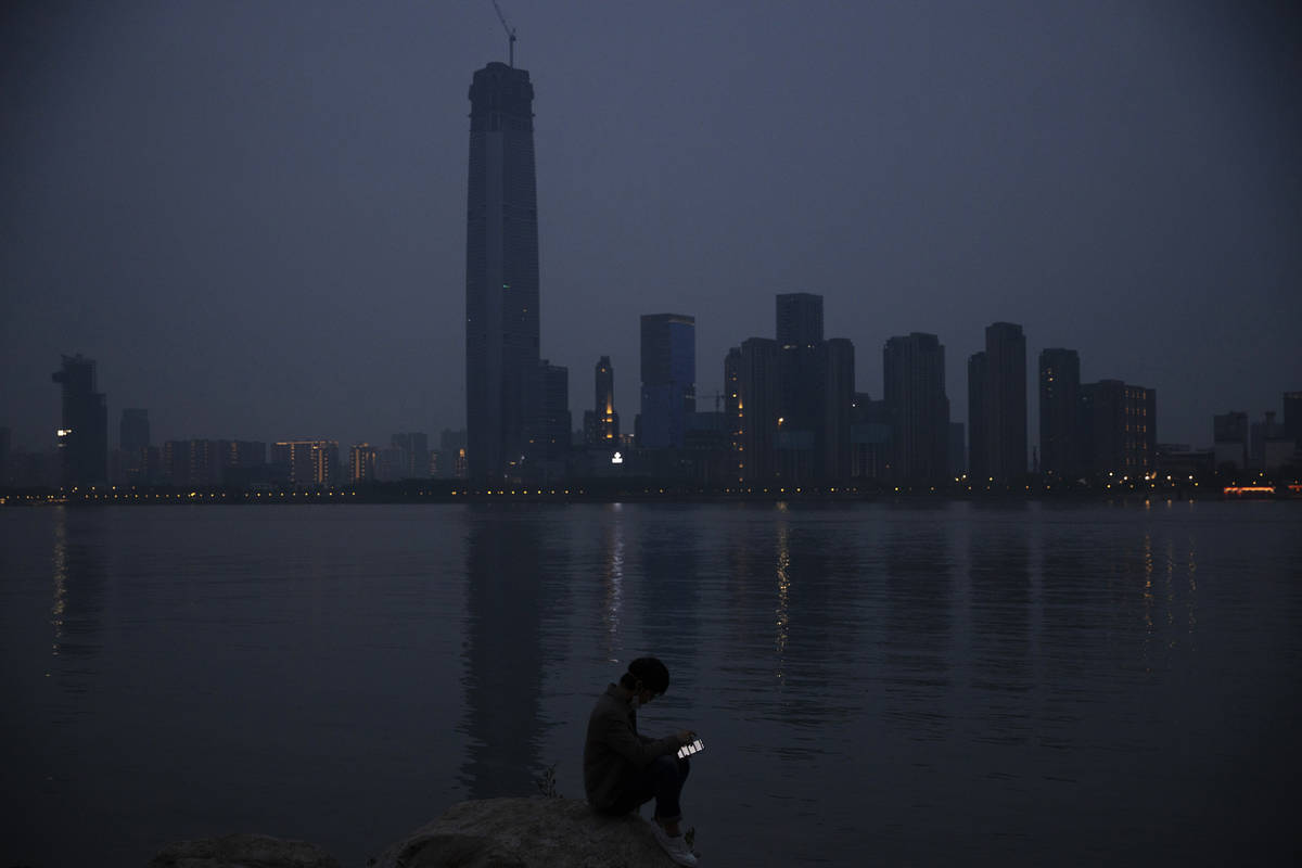 In this April 5, 2020, file photo, a man checks his mobile phone along the Yangtze River in Wuh ...