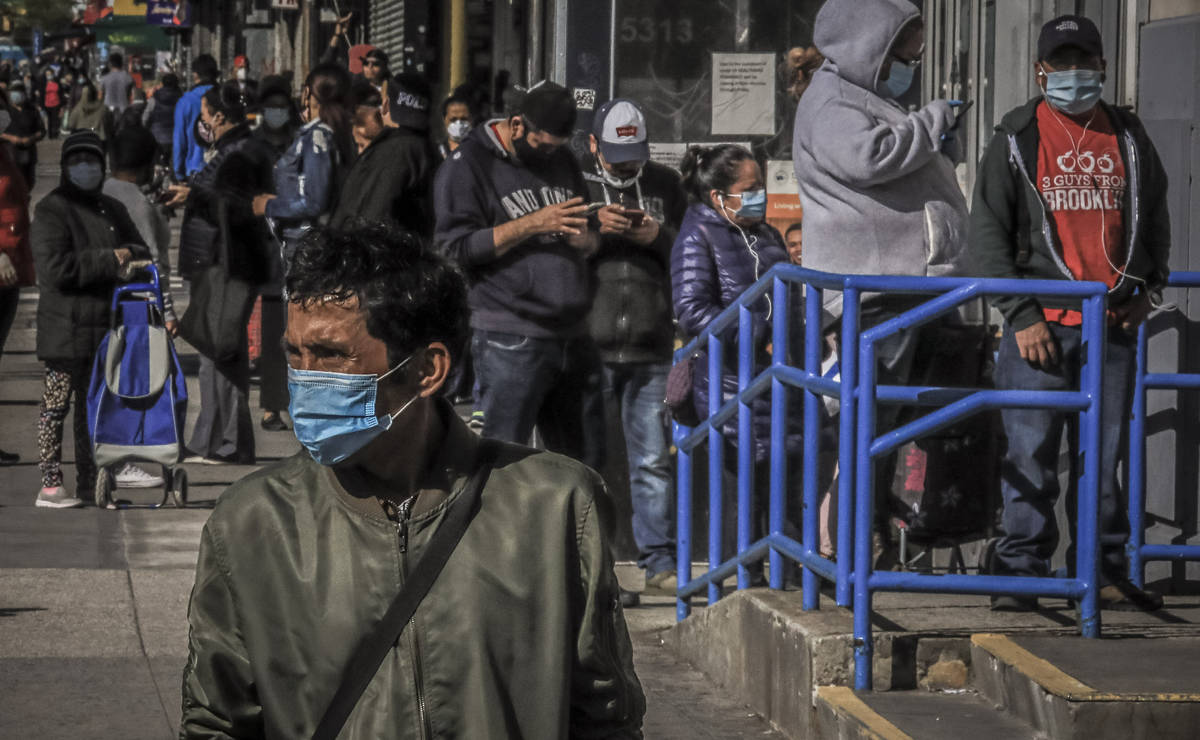 A masked pedestrian waits to cross a street after walking past a line of people in Brooklyn's S ...