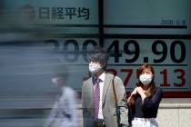 People wearing a face mask to help curb the spread of the coronavirus stand near an electronic ...