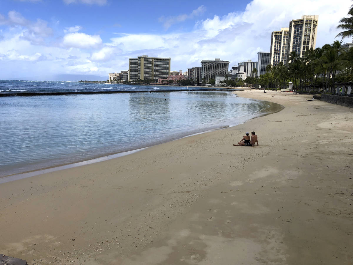 FILE - In this March 28, 2020, file photo, a couple sits on an empty section of Waikiki Beach i ...