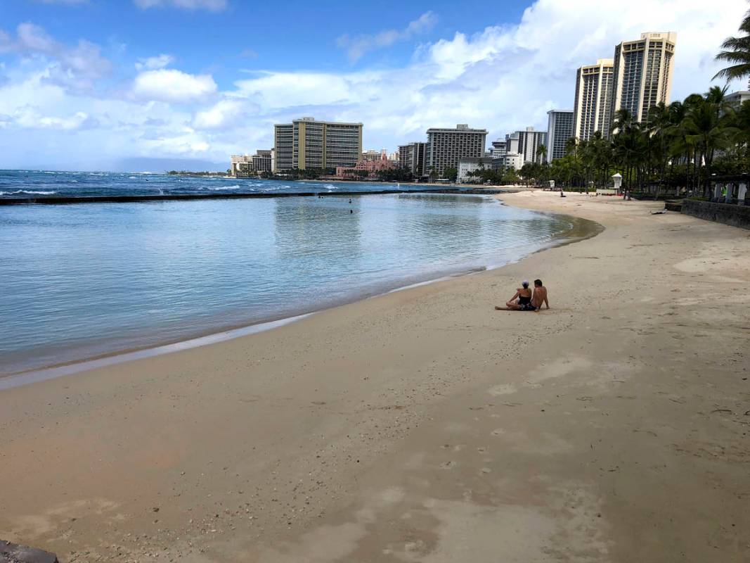 FILE - In this March 28, 2020, file photo, a couple sits on an empty section of Waikiki Beach i ...