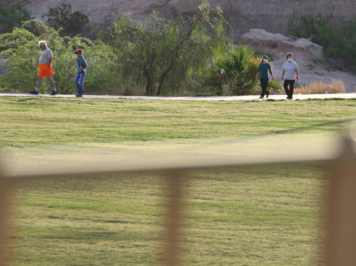 People walk while practicing social distancing during a cool and windy morning at Charlie Frias ...