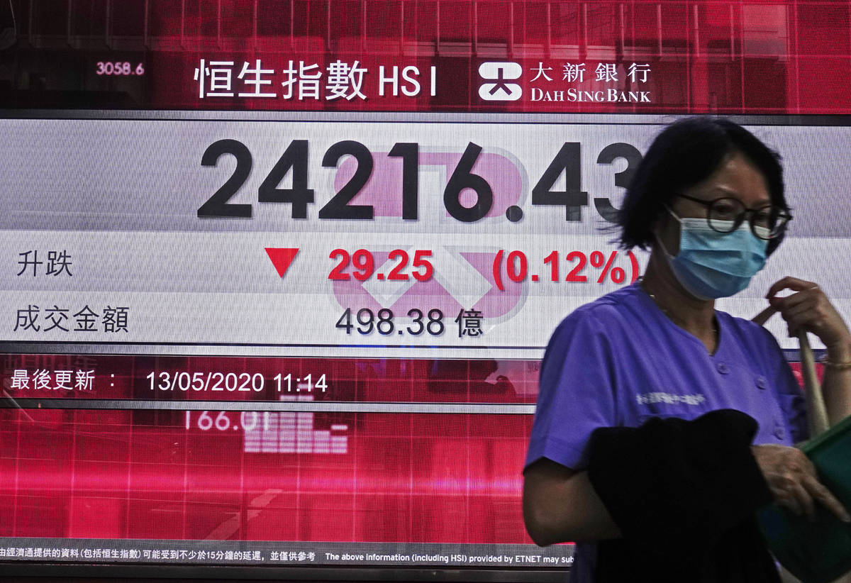 A woman wearing face mask walks past a bank electronic board showing the Hong Kong share index ...