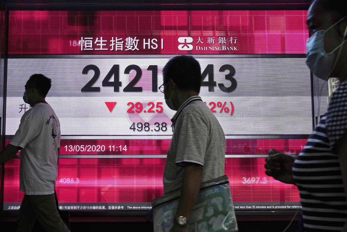 People wearing face mask walk past a bank electronic board showing the Hong Kong share index in ...