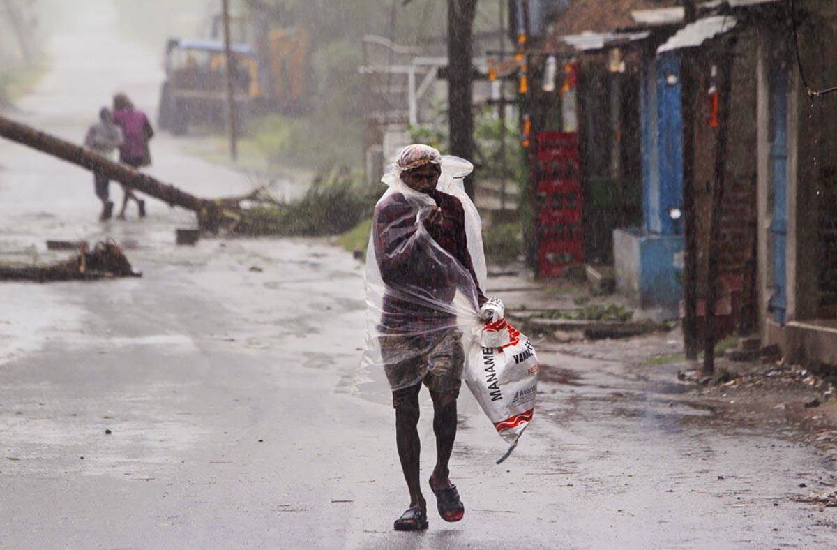 A man covers himself with a plastic sheet and walks in the rain ahead of Cyclone Amphan landfal ...