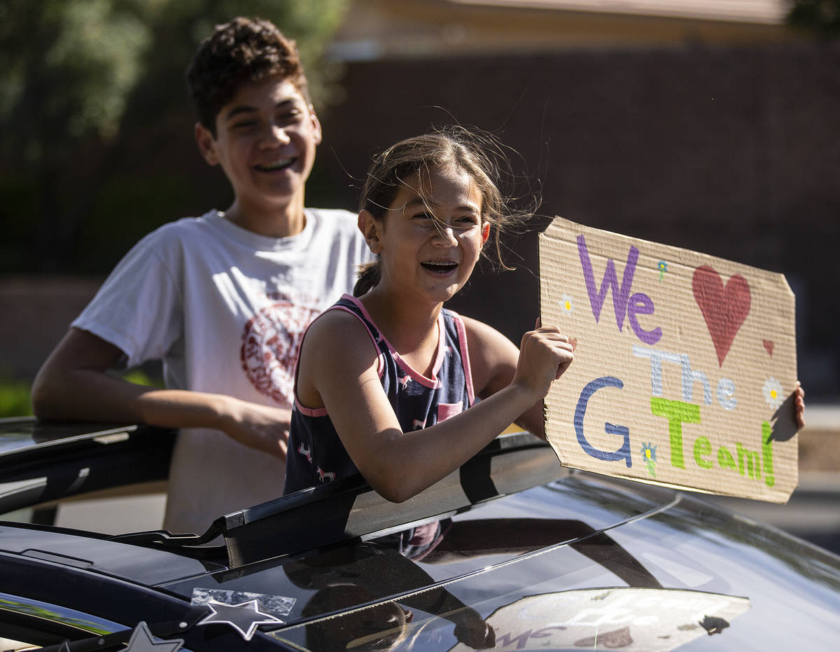Children hold signs sending well wishes in a line of cars during a “drive-by” ret ...
